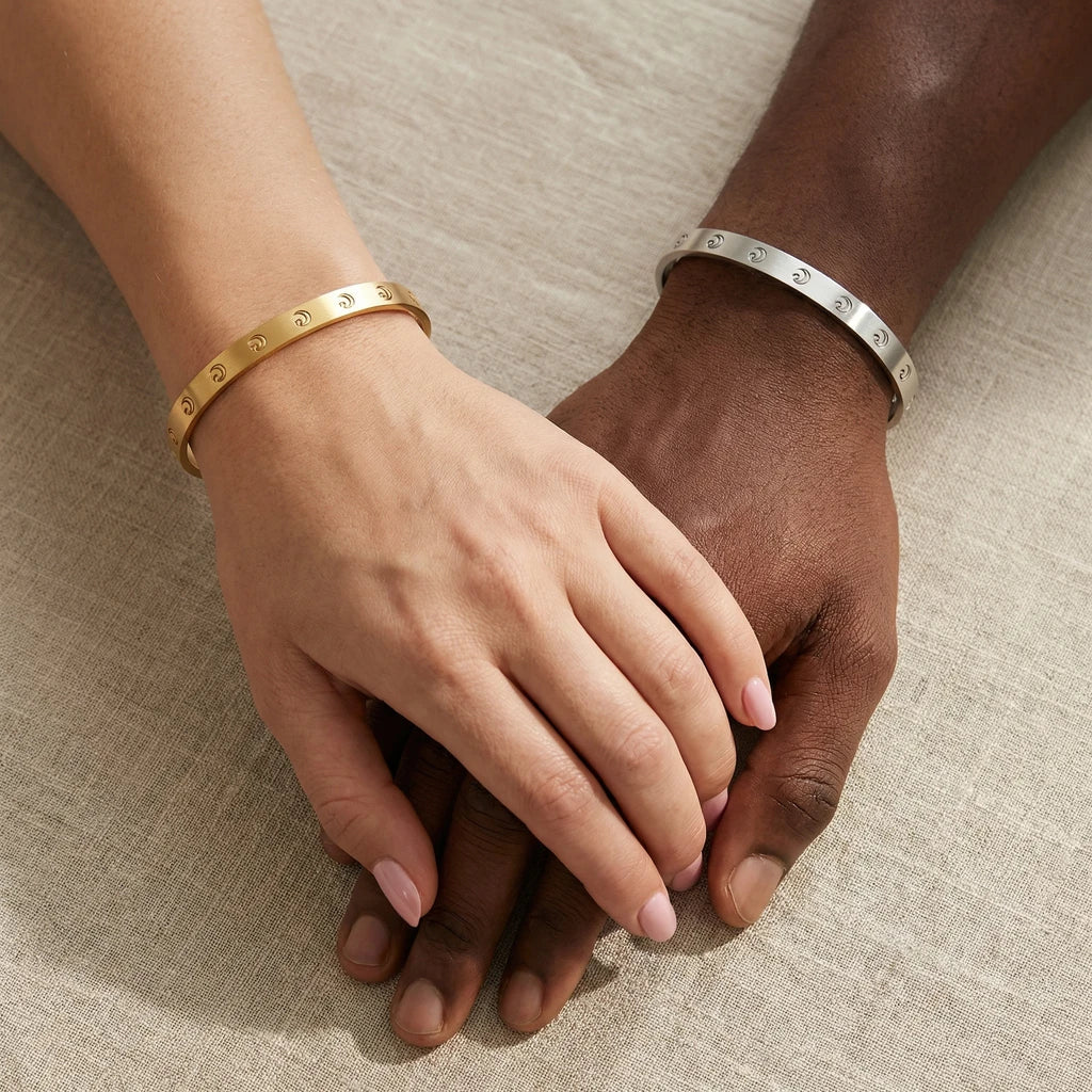 A close-up of two people with different skin tones holding hands while wearing matching patterned bracelets.